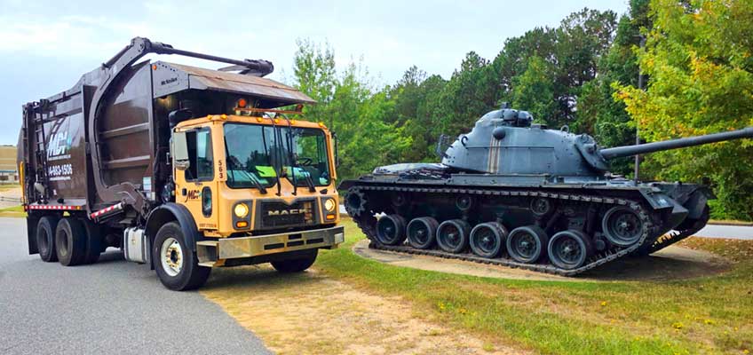 MDI front load garbage truck parked next to a military tank at Ft Benning, GA.